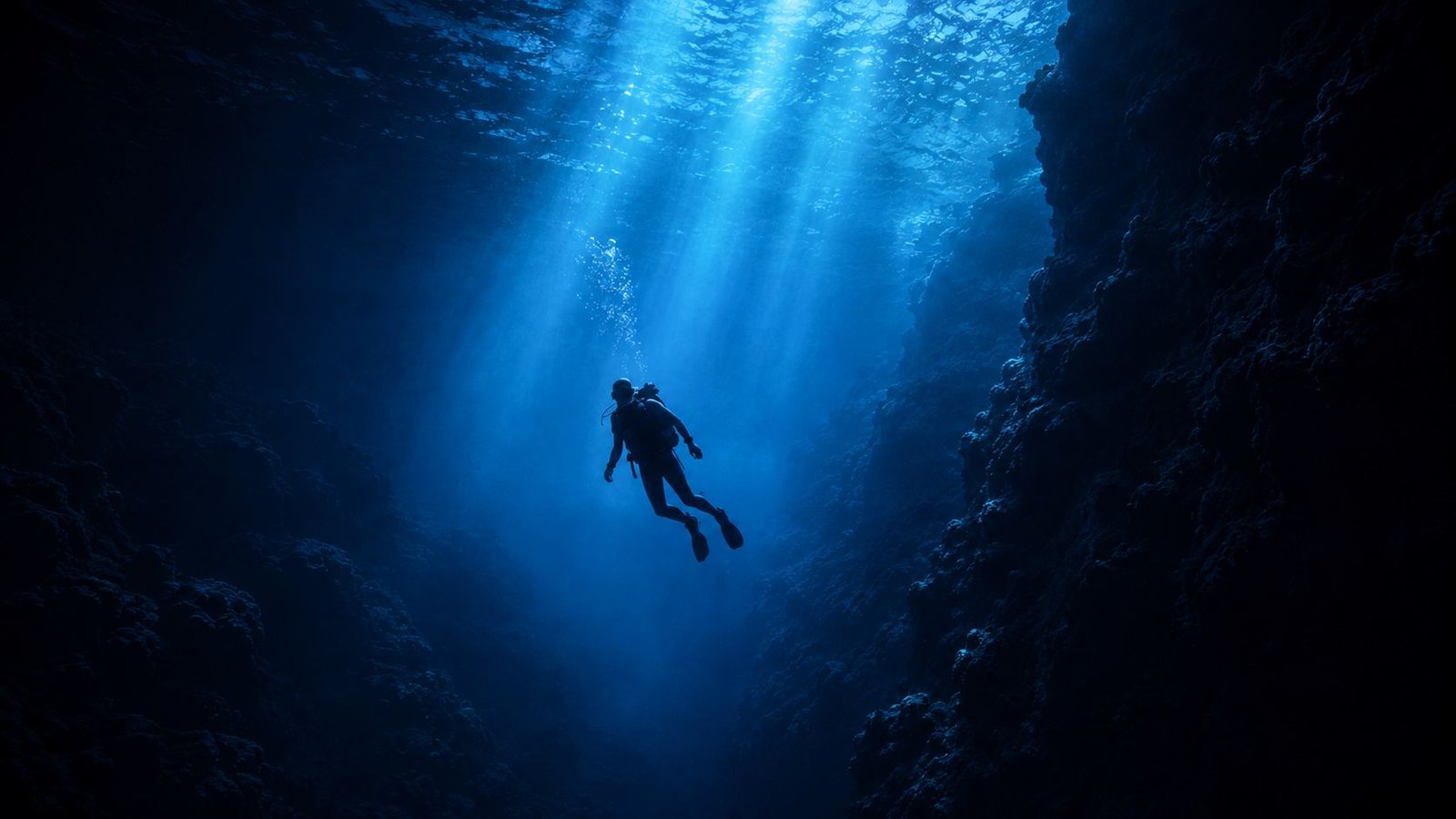 Mergulhador descendo por um desfiladeiro submerso iluminado por feixes de luz